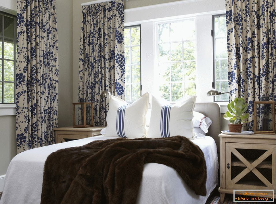 Blue flowers on the curtains and stripes on the pillows are harmoniously combined in the interior of the bedroom