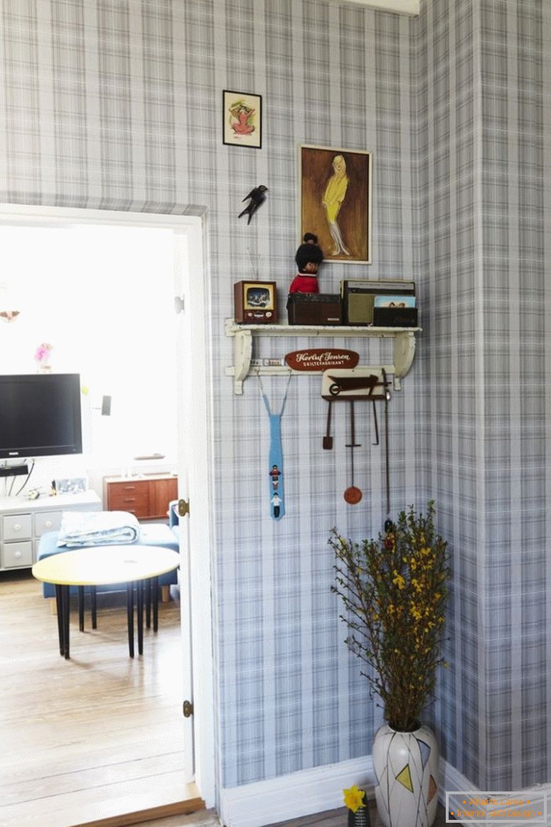 Hallway with checkered wallpaper, floor vase under wallboard, next to open door to living room