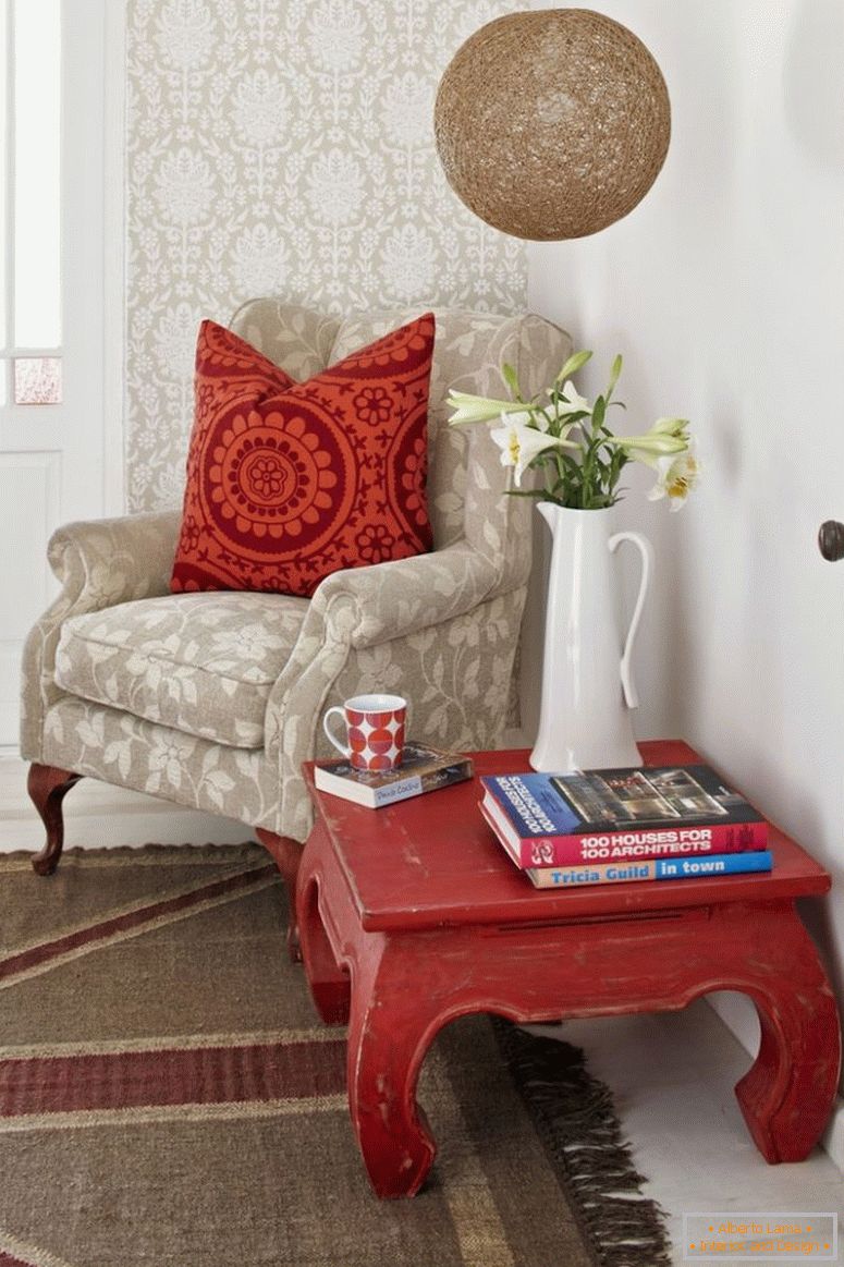 Reading corner; opium table and pale armchair with patterned scatter cushions against wallpapered wall