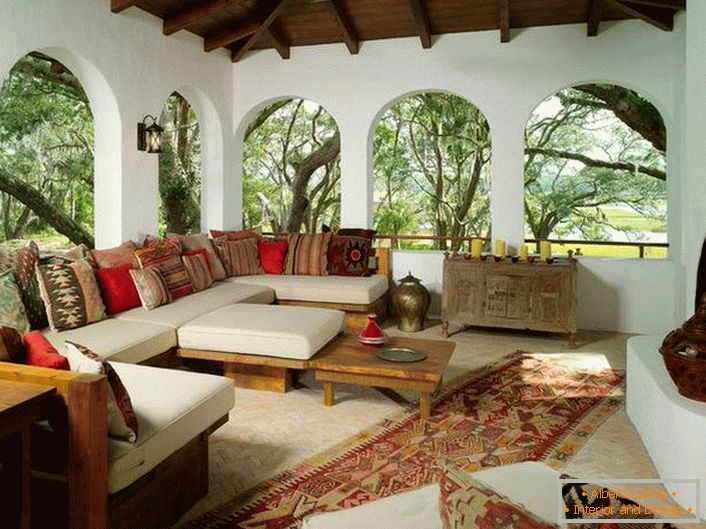 The verandah of the country house is decorated in accordance with the Mediterranean style. An interesting feature is the decor with a lot of colorful cushions.