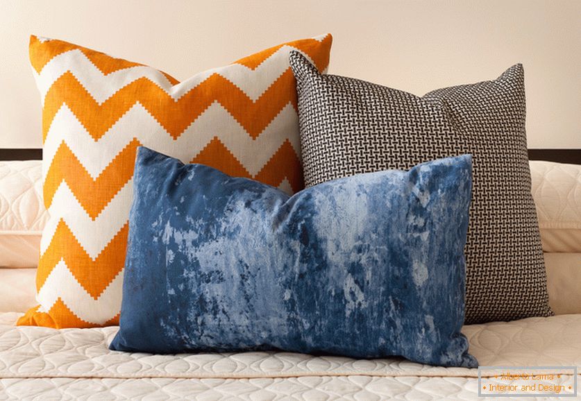 Bright orange, blue and black-and-white decorative cushions with interesting prints on the bed