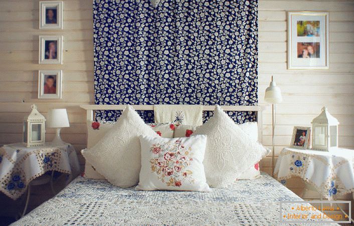 In accordance with the rustic style, the bed is decorated with a number of pillows with contrasting red embroidery. Bedside tables are covered with a tablecloth with delicate blue flowers.