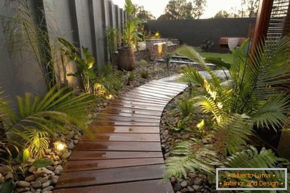 Wooden paths with pebbles and backlighting near the house