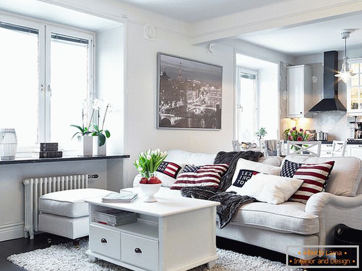 A cozy studio apartment in Scandinavian style is decorated mainly in white. Windows without curtains allow enough daylight to enter the room.