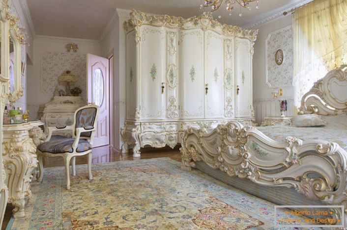 Snow-white bedroom with carved massive furniture made of wood. The bed with a high headboard at the headboard, elegantly fits into the interior in the Baroque style.