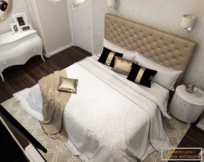 In the center of the design composition is a bed with a high, upholstered soft headboard material. The pompous art-deco style manifests itself in the use of expensive fabrics for decor, so on the bed we see pillows with satin pillowcases and chic bed linens.
